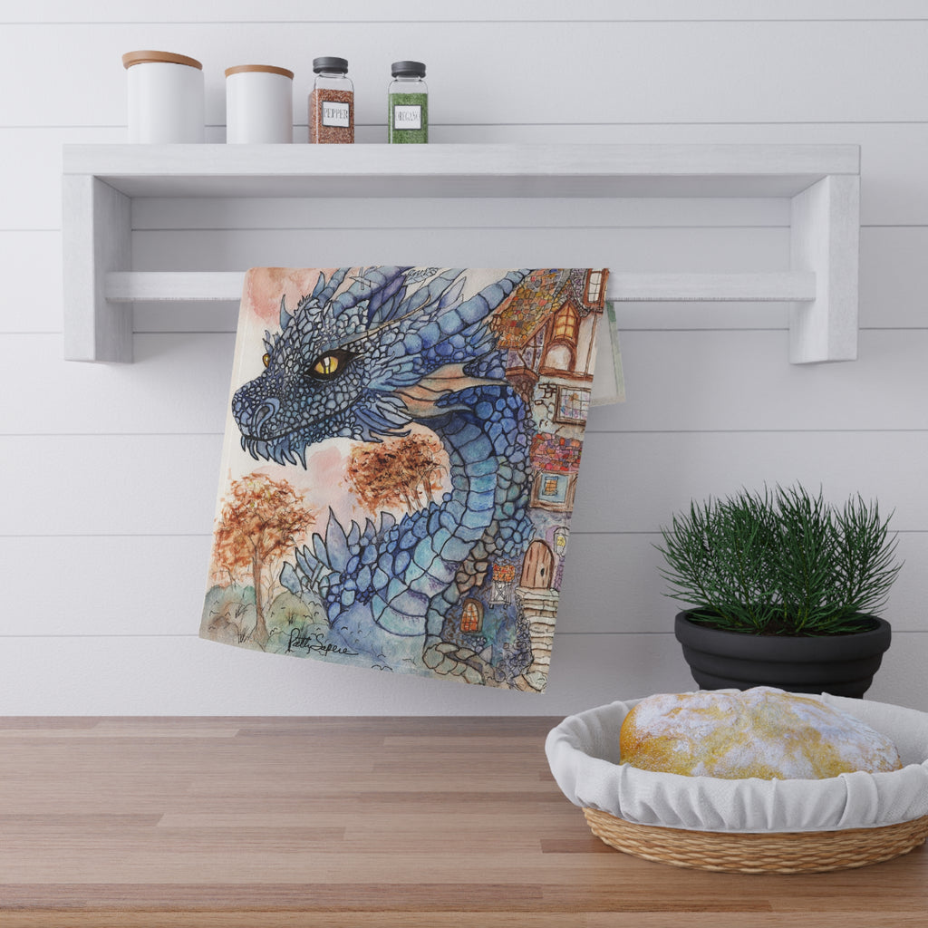 Cotton kitchen tea towel with a watercolor blue dragon beside an autumn cottage with warm golden light and fall foliage by Patty Sapere, hanging in a farmhouse kitchen